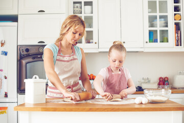 Rolling out the dough. Cute little girl baking in the kitchen with her mom.