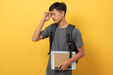 Smiling young college student with books and backpack isolated on yellow background suffering from headache and stressed