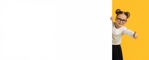 Educational Ad. Schoolgirl Peeking Behind Blank Advertisment Board And Showing Thumb Up