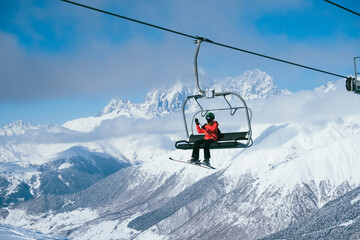 Skier sitting on Chair ski lift at ski resort against backdrop of amazing mountain peaks covered...