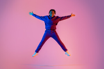 Fototapeta na wymiar Full body length of sporty african american young woman jumping up in star shape, having fun over pink neon background