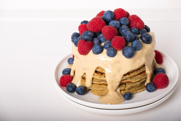 Delicious freshly cooked thick and fluffy protein pancakes stacked on white plate, served with cashew cream and fresh berries. Healthy food, low carb diet.