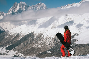 Snowboarder woman standing with snowboard beautiful mountain peaks covered with snow on background