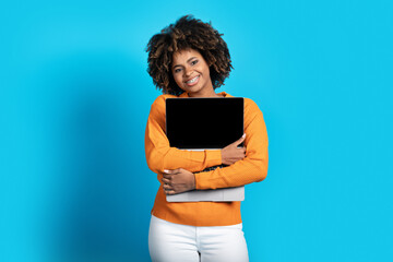 Cheerful african american lady embracing laptop with blank screen