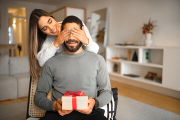 Happy millennial european woman closes eyes to arabian guy, gives box with gift, celebrating holiday