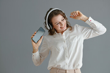 Portrait of positive middle-aged woman dancing to music from playlist on her smartphone