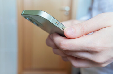 Side view. Hand of man or woman using smartphone in the living room at home, typing message, texting or scrolling the news, shopping. Close-up of hands. High quality horizontal photo.