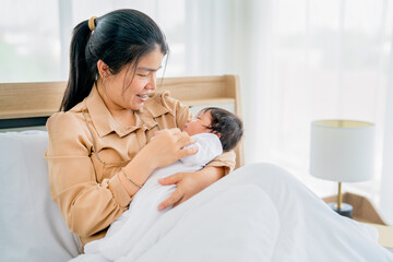 Close up Asian mother hold newborn baby and sleep on her chest and sit on bed in bedroom with day light and take care also look with love and happiness.