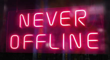 Fototapeta na wymiar Pink neon sign with the text ' never offline ' against a dark background. Capital letters in clear writing glow in a dark shop window.