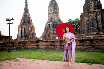 Beautiful Thai girl in traditional dress costume red umbrella as Thai temple where is the public place, Thai Woman in Traditional Costume of Thailand.