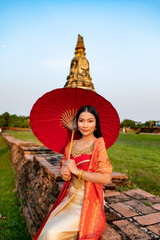 Beautiful Thai girl in traditional dress costume red umbrella as Thai temple where is the public place, Thai Woman in Traditional Costume of Thailand.