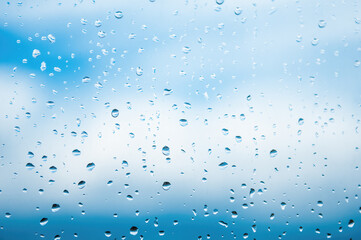 Raindrops on window glass against blue sky with white clouds. Place for text banner