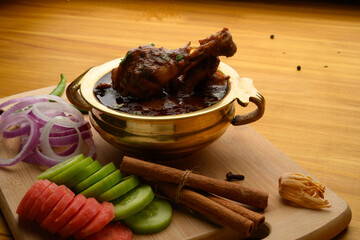 Spicy Reddish saoji Chicken Curry  Masala served in brass bowl or Kadhai ,with prominent Leg Piece, different spices and salad like cucumber onion carrot over  wooden background.