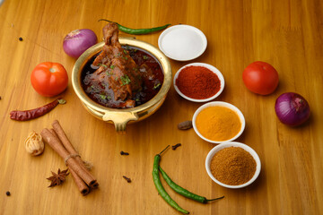 Spicy Reddish saoji Chicken Curry  Masala,with prominent Leg Piece, different spices served in brass bowl or Kadhai over  wooden background.