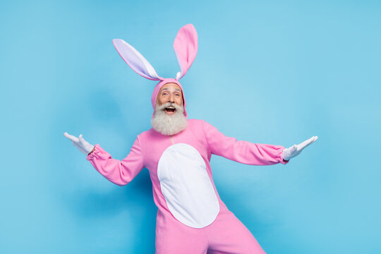 Photo of positive charming man pensioner dressed pink rabbit nightwear dancing smiling isolated blue color background