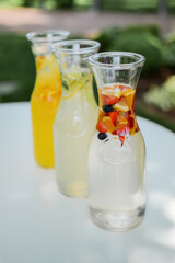A variety of lemonade in glass jars with berries and fruits on a white table in the garden