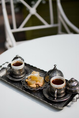 A cup of coffee with a balaclava on a metal oriental tray with sweets. Turkish coffee outside on a white table