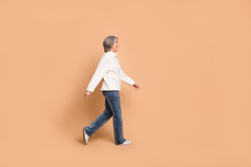 Fototapeta na wymiar Full length photo of funky adorable lady dressed white sweater walking looking empty space isolated beige color background