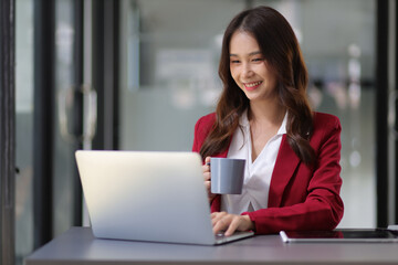 Young beautiful asian businesswoman in happy office smiling hopeful and thinking about future success.