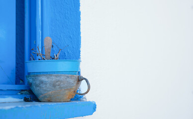 Blue stone windowsill and a metal mug with a flower pot, internal details of a typical Greek house, a white stone wall with text for text or the idea of a background