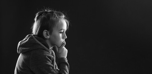 Sad young boy thinking about his problems. Afraid child sitting quiet in dark. Young boy suffering from anxiety.