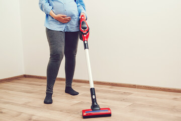 Young pregnant woman enjoys cleaning her house. Modern easy cleaning. Easy cleaning with a wireless vacuum cleaner.