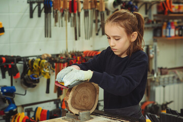 Cute boy makes wooden clock in the workshop. Young carpenter working with wood and sandpaper in craft workshop.