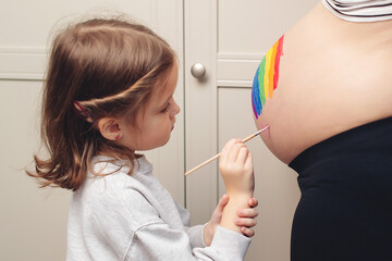 Sweet little daugter painting pregnant belly her mother. Baby birth expecting time and belly painting.