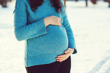 Pregnant woman's belly over winter background. Pregnant woman in blue sweater touching big belly with hands.