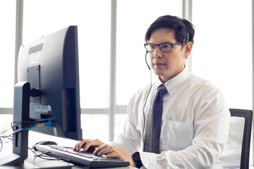 Obraz na płótnie Canvas Customer service call center. Attractive asian male operator with headset smiling and talking help customer who complaint at workplace center office.
