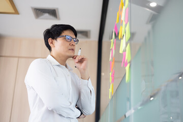 Asian office worker thoughtful about new project presentation, putting plan and idea at sticky...