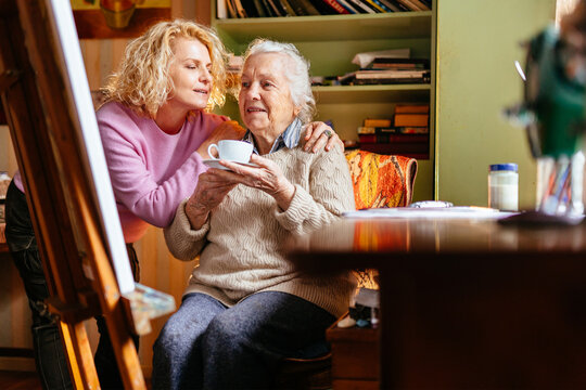 Caring middle-aged daughter serving cup of tea to her beloved elderly mother.