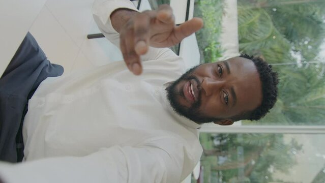 Vertical format video of black male blogger smiling and talking on camera as streaming from outdoor cafe at daytime