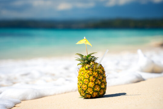 Decorated Pina Colada cocktail in natural pineapple on the white sand of the tropical beach. The turquoise sea wave in the background. Best Summer Vacation in the resort