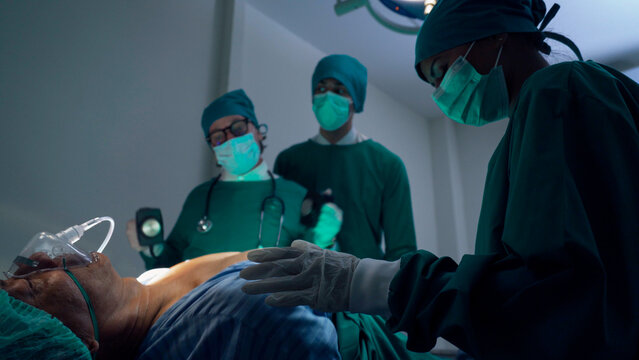 Doctor using defibrillator to pump at chest of patient to save life while doing medical surgery in operating room. 