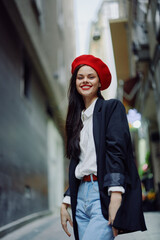 Fashion woman smile with teeth portrait walking tourist in stylish clothes in jacket with red lips walking down narrow city street flying hair, travel, cinematic color, retro vintage style.