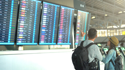 Couple traveler checking flight schedule board in airport terminal.