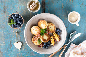 Cottage cheese pancakes, cheesecakes, ricotta fritters with fresh blueberries, currants and peaches on a plate. Healthy and delicious breakfast for the holiday. Blue wooden background