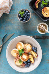 Cottage cheese pancakes, cheesecakes, ricotta fritters with fresh blueberries, currants and peaches on a plate. Healthy and delicious breakfast for the holiday. Blue wooden background