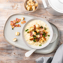 Cheese leek soup with croutons and bacon in a bowl on a wooden table.