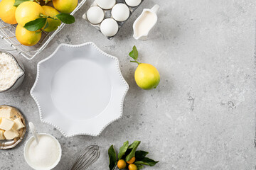 White ceramic cake pan with lemons. Ingredients for making a lemon curd pie on a white stone table.