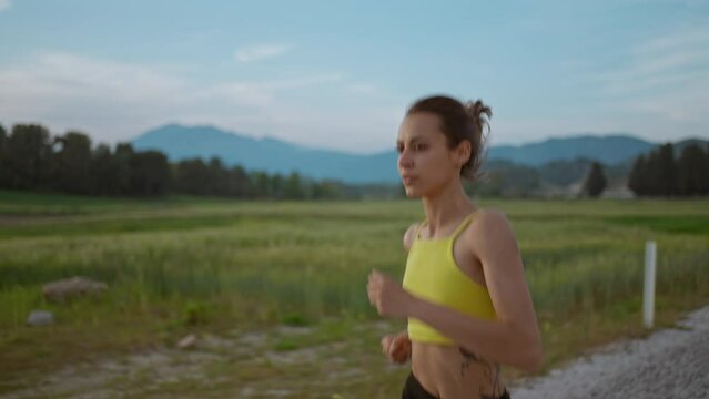 slow motion portrait of Young Athlete Woman Running Fast down Road, Training Hard, Getting Ready for Race Competition or Marathon. Fit Girl in Black shorts Jogging At Dawn along Green Fields.
