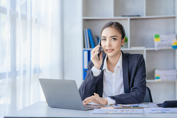 Freelance asian businesswoman talking on the phone and working with laptop computer and financial graph document manage her business at work Make a plan about financial reports in the office.