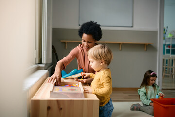 Happy black teacher and little boy play with puzzles at kindergarten.