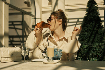 A adult woman takes a bite out of a piece of croissant