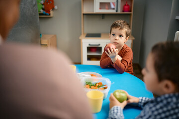 Small boy eats an apple after lunch at preschool.