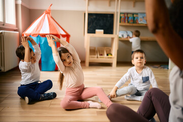 Group of kids exercising with their teacher at preschool. - obrazy, fototapety, plakaty