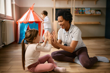 Happy African American teacher and little girl play clapping game at kindergarten.