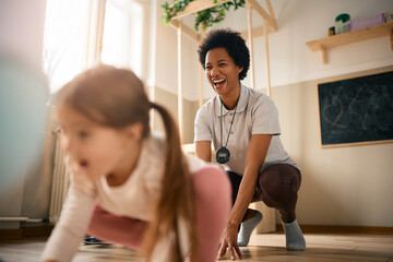 Happy black teacher PE teacher has fun with children while exercising at kindergarten.