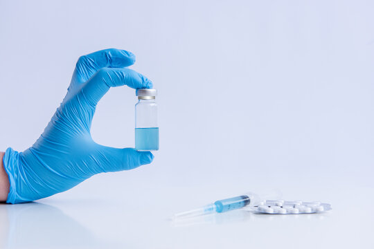 On white isolated background, hands of doctor in medical blue gloves hold ampoule vaccine against virus